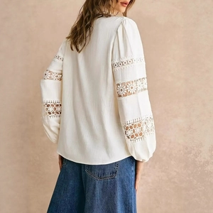 Detail of white long sleeve shirt showing intricate lace stitching and cotton texture