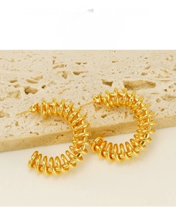 Detailed view of polished gold spring-shaped C-style hoop earrings on textured stone