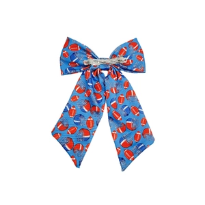 Close-up of blue bow hair clip with red rugby and helmet patterns on a white background