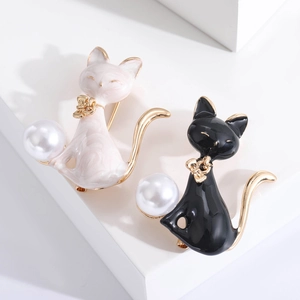Chic cat brooches in black and white enamel with gold accents and pearls on a white background