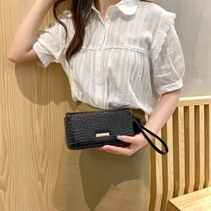 Elegant black crocodile pattern long zip wallet with wrist strap held by a model