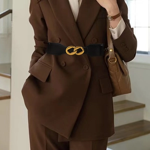 Women's black elastic waist belt with gold double ring buckle styled over a brown blazer