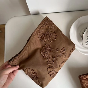 Detailed close-up of dark brown suede makeup bag featuring exquisite daisy floral embroidery