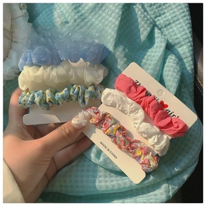 Close-up of six floral chiffon scrunchies set on white display cards held by hand