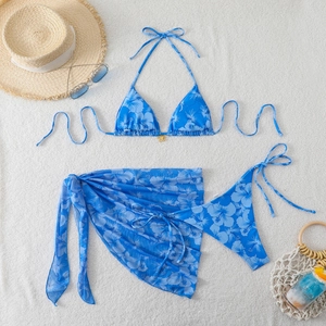 Detailed flat lay of blue floral 3-piece bikini with gold butterfly charm and beach sarong