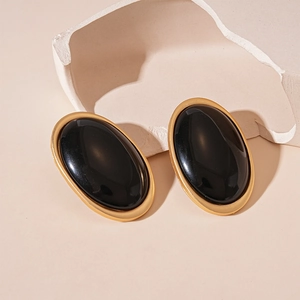 Vue détaillée de boucles d'oreilles ovales en résine noire avec bords dorés sur pierre