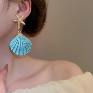 Detail view of a gold starfish and blue shell drop earring worn by a female model