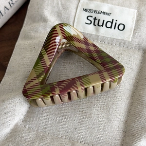 Détail d'une pince à cheveux vintage à carreaux rouge et vert sur un fond en toile beige