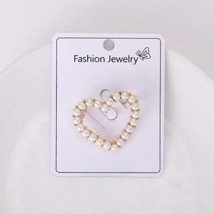 Close-up of heart-shaped brooch with white pearls and gold alloy base on a card