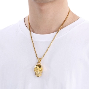 Close-up of golden gothic skull pendant worn on a chain against a white shirt background