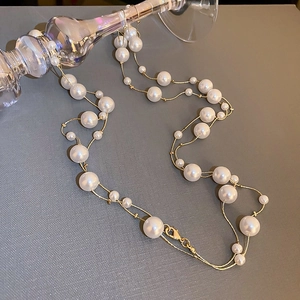 Detail einer eleganten Goldkette mit verschieden großen weißen Perlen auf Glas-Display