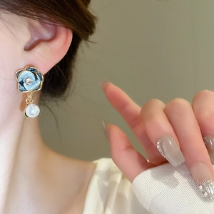 Detail of elegant enamel flower earring with pearl drop on a model showing realistic size