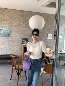 Detail of a purple woven bucket bag held by a model in a French casual cafe setting