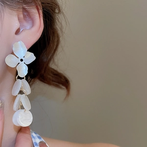 Macro view of creamy white pearlized petal earrings with golden metal links on a model