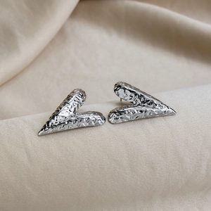 Detail of V-shaped silver earrings with hammered texture on beige satin fabric