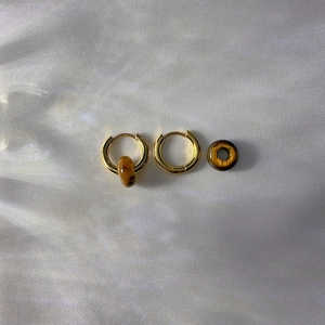 Detailed macro of golden hoop earrings with natural tiger eye stone beads on silk fabric