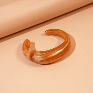 Detailed view of amber acrylic bangle with marble texture on warm minimalist background