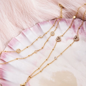 Macro shot of 18k gold double-layer chain bracelet with heart and zircon pendants