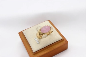 Detail of pink cabochon gemstone ring on a wooden display stand with golden band
