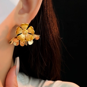 Macro shot of stylish gold metal flower earrings worn by a model on black background