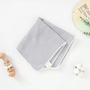 Détail d'une serviette en mousseline grise pour bébé avec bordure à pompons blancs