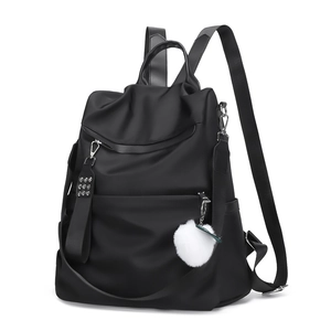 Minimalist black nylon backpack with white plush ball charm and multiple zip pockets