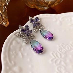 Détail de boucles d'oreilles fleurs avec gemmes violettes et pierres en goutte sur céramique blanche