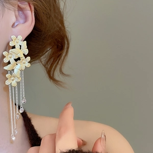 Detail of long gold tassel earrings with intricate flower butterfly motifs worn by a model