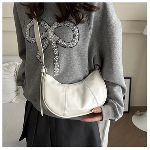 Close-up of a cream white half-moon leather crossbody bag worn by a model in a room