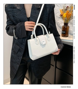 Close-up of white square handbag with crocodile pattern flap and reinforced corners