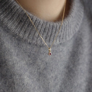 Golden necklace with a red zircon pendant worn on neck for a minimalist jewelry look
