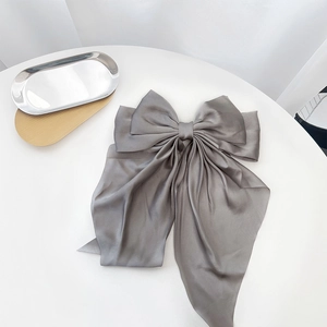 Detail view of a gray silk bow hair clip on a minimalist metal tray with a soft satin finish