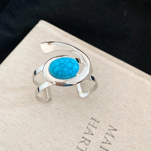 Detail of silver spiral open cuff bracelet with oval turquoise stone on book background