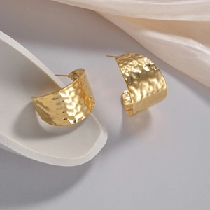Detailed view of golden wide C-shaped earrings with hand-hammered metal texture