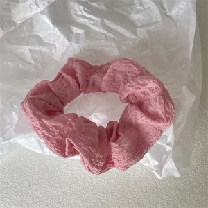 Detail eines rosa plissierten Haargummis mit Chiffon-Textur auf weißem Papier