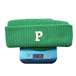 Lichtgroene gebreide muts met witte P-letterpatch op een weegschaal die 86g weegt