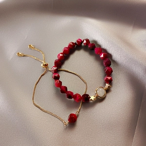 Detail of red beaded star bracelet and gold chain set on elegant grey silk fabric