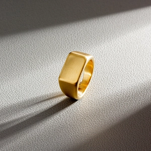Macro detail of square signet ring in matte gold finish with brushed texture on leather