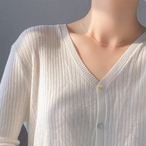 Détail d'un collier minimaliste en perles dorées avec un cardigan blanc