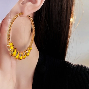 Detail of large gold hoop earring with yellow gemstones and crystals on a model