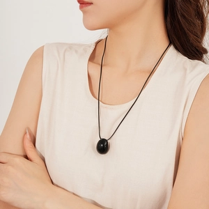 Gros plan d'un pendentif ovale noir minimaliste sur un cordon de cire porté par un modèle