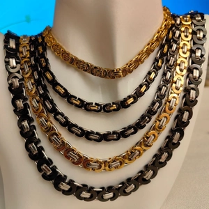 Close-up of Byzantine chain necklaces in gold, black, and silver on a white mannequin