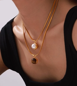 Detail of double-layer gold titanium necklace with tiger eye stone and shell pearl charms