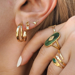 Macro detail of gold earrings and ring set with green gemstones and zircon accents
