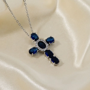 Detailed macro of a silver cross pendant with oval dark blue zircons on champagne silk