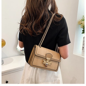 Detail of beige snakeskin shoulder bag featuring golden bee clasp with white pearls