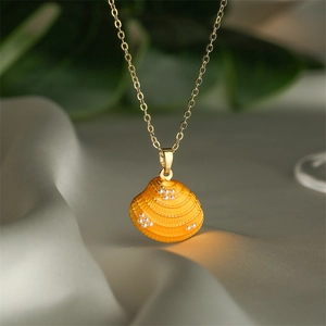 Detalle de colgante de concha bañada en oro con esmalte naranja y pequeñas perlas finas