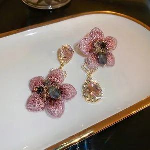 Asymmetric flower earrings with pink and purple petals and teardrop crystals on a white plate