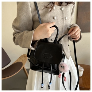 Mini zaino nero in pelle con ciondolo di peluche rosa indossato su giacca in tweed