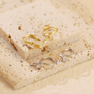 Close-up of gold and silver bow drop earrings with sparkling rhinestones on travertine